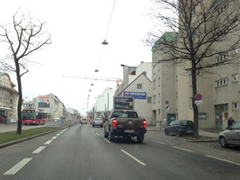Straße, zu sehen eine zweispurige Fahrbahn in eine Richtung, links daneben ein Gleiskörper mit Bus und Haltestellen